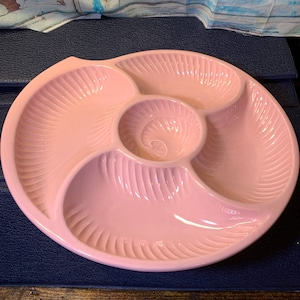 Puede incluir: Un plato de servir de cerámica rosa con cuatro secciones. El plato tiene un borde festoneado y un diseño de espiral en el centro.