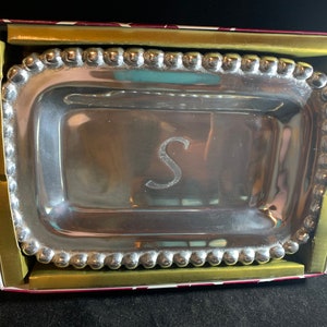 Puede incluir: Una bandeja rectangular de servir plateada con un borde de cuentas y la letra "S" grabada en el centro. La bandeja está en una caja roja y dorada.