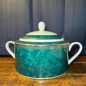 May include: A covered sugar bowl with a green marble-like pattern and gold trim. The bowl has two handles and a white knob on the lid. The sugar bowl is made of ceramic.