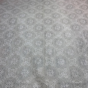 Puede incluir: Una tela gris grande con un patrón repetitivo de diseños florales dentro de marcos cuadrados. El patrón es de un tono gris más claro, creando un contraste sutil. La tela parece suave y fluida.