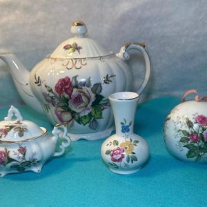 Puede incluir: Un juego de cuatro tazas de té de porcelana blanca con diseños florales. El juego incluye una tetera, un azucarero, un jarrón y un adorno redondo.