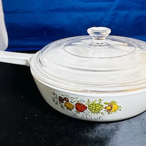 May include: White casserole dish with a clear glass lid and a white handle. The dish features a colorful vegetable design with the text "Le Persil" on the side. The dish is likely for cooking and serving.