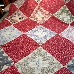 May include: A patchwork quilt featuring a repeating pattern of solid red floral squares alternating with white squares containing various floral prints and handwritten names and dates in ink, including Allen Sligar 1931 and Margaret Sligar 1931.