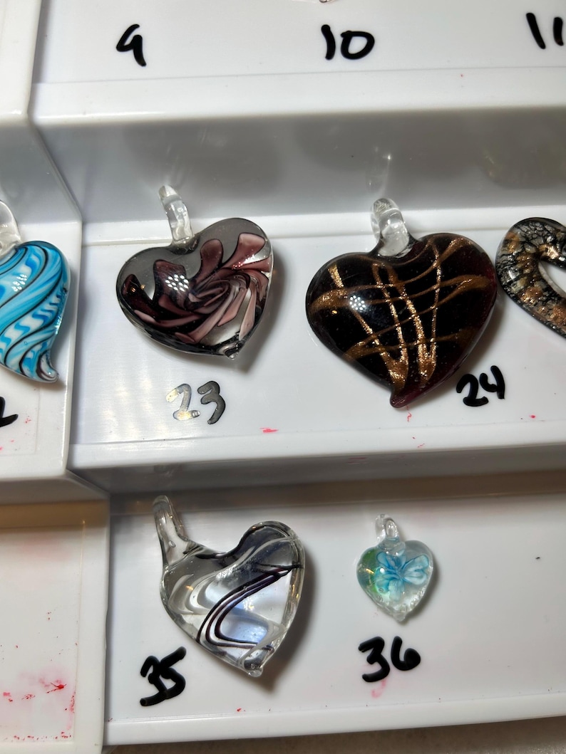 May include: A collection of heart-shaped glass pendants in various colors and designs. One pendant features a swirling pattern of pink and gray, another has gold lines on a black background, and a third has a blue butterfly.