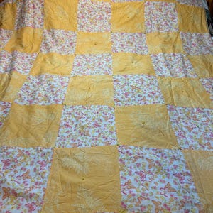 May include: A patchwork quilt featuring an alternating grid of solid yellow squares with a subtle fern leaf pattern and white squares decorated with a colorful butterfly and floral print. The quilt is tied with small yellow thread knots.