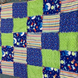 May include: A patchwork quilt featuring squares of blue, green, and striped fabric. The blue squares have white polka dots or sea creature designs. The quilt is a mix of textures and colors, suitable for a baby or child.