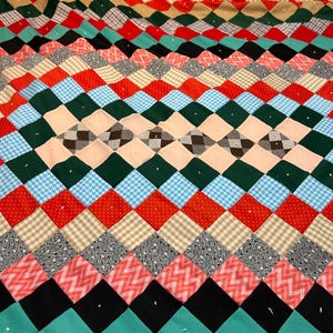 以下が含まれることがあります： ダイヤモンド模様のカラフルなパッチワークキルト。赤、緑、青、黒、タンの様々な生地を使用。水玉模様、チェック柄、その他の幾何学模様のデザインが含まれています。