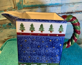 May include: A blue and white ceramic pitcher with a green and red twisted handle. The pitcher has a white background with a blue and gold polka dot pattern. The top of the pitcher has a row of green Christmas trees. The bottom of the pitcher has the word "LOVE" spelled out in colorful blocks.
