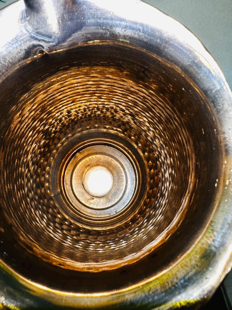 May include: An overhead view inside a metal container. The interior is a series of concentric rings, with a central light source. The metal has a tarnished, aged appearance with shades of brown and silver.