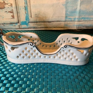 Puede incluir: Plato de cerámica blanco con asas plateadas y un diseño de rejilla. El plato tiene un borde negro y tiene forma de barco.