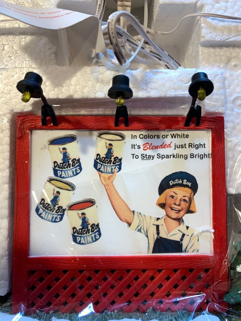 May include: A red wooden sign with a white background and a framed advertisement for Dutch Boy Paints. The sign features a young person holding a can of paint and the text "In Colors or White It's Blended just Right To Stay Sparkling Bright!"