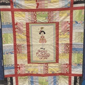 May include: A patchwork quilt featuring a central panel with an illustration of a person holding a flower and the text "FRIENDS ARE THE FLOWERS IN THE GARDEN OF LIFE." The quilt is composed of various patterned fabric blocks in red, yellow, blue, and green.