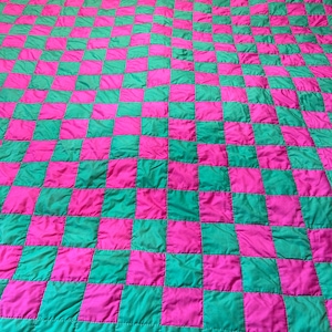 May include: A large, quilted blanket with a checkerboard pattern. The squares alternate between bright pink and teal green. The blanket has a teal green border and a pink trim.