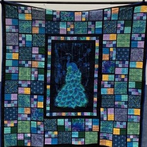 May include: A rectangular quilt featuring a central panel with a peacock illustration in shades of blue and green, surrounded by a border of smaller, multi-colored fabric squares in various patterns of teal, navy, yellow, and purple.