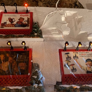 May include: Four miniature lighted billboards with holiday scenes. The first billboard advertises Campbell's Soup with the text "Any season, any weather, Soup is crackers together". The second billboard advertises "The difference between "Dry and "Nice". The third billboard advertises "Paints" with the text "In Colors or White, It's "Bleach" just right to stay sparkling bright". The fourth billboard advertises "Paints" with the text "In Colors or White, It's "Bleach" just right to stay sparkling bright".