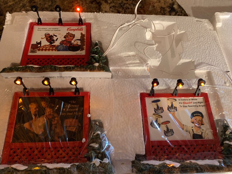 May include: Four miniature lighted billboards with holiday scenes. The first billboard advertises Campbell's Soup with the text "Any season, any weather, Soup is crackers together". The second billboard advertises "The difference between "Dry and "Nice". The third billboard advertises "Paints" with the text "In Colors or White, It's "Bleach" just right to stay sparkling bright". The fourth billboard advertises "Paints" with the text "In Colors or White, It's "Bleach" just right to stay sparkling bright".