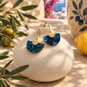 May include: A pair of gold-tone drop earrings featuring semi-circular pendants with a marbled blue and teal resin finish. Each earring has a textured gold-tone metal accent at the top where the hook attaches, creating a fan-like shape.