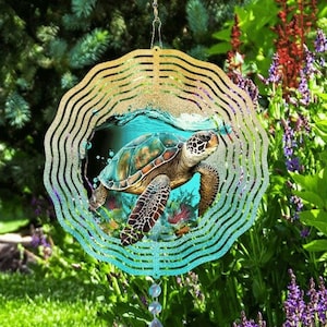May include: A colorful metal wind spinner with a sea turtle design. The spinner has a layered, circular design with a blue, green, and yellow color scheme. The turtle is depicted swimming in the ocean with bubbles and coral.