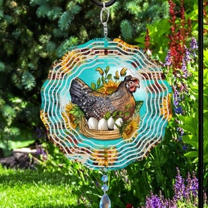 May include: A colorful metal wind spinner with a design of a hen sitting on a nest of eggs surrounded by sunflowers. The spinner has a turquoise background with white and red accents.