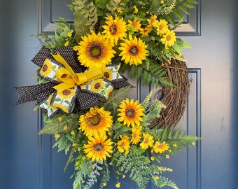 May include: A sunflower wreath with a black and white polka dot bow. The wreath is made of grapevine and features a variety of sunflowers, greenery, and small yellow flowers.