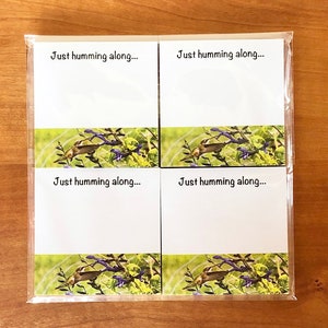 May include: Four white note cards with a hummingbird and flowers design. Each card has the text "Just humming along..." printed on it.