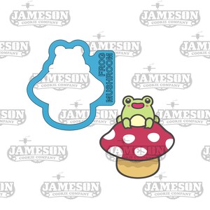 May include: A green frog sitting on a red and white mushroom with white dots. The mushroom has a brown stem. The image includes a blue cookie cutter in the shape of a frog on a mushroom.
