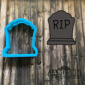 May include: Blue plastic cookie cutter shaped like a tombstone with the word "RIP" on it. The cookie cutter is on a wooden background.