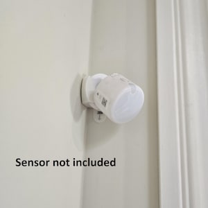 May include: A white security light fixture mounted on a corner wall. The fixture has a rounded shape with a clear, domed lens. The text "Sensor not included" is displayed below the fixture.