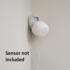May include: A white smart home sensor with the brand name "Aqara" is mounted on a wall. The sensor is connected to a white wall outlet. The text "Sensor not included" is displayed below the sensor.
