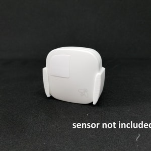 May include: White wireless smart home sensor with a small bee logo. The sensor is mounted on a white wall mount. Sensor not included.