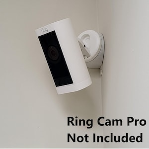 May include: White Ring security camera mount with the text "Ring Cam Pro Not Included" on a white wall.