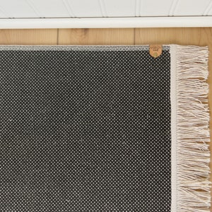 May include: Black and white patterned rug with a white fringe border. The rug has a small brown leather tag with the text "Made in USA" on it.