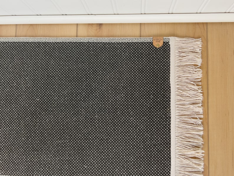 May include: Black and white patterned rug with a white fringe border. The rug has a small brown leather tag with the text "Made in USA" on it.