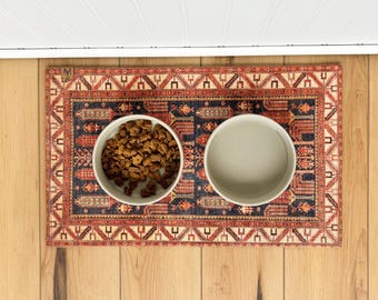 May include: Two round, light-colored ceramic bowls placed on a rectangular mat featuring a dark blue and red intricate geometric pattern. One bowl contains brown, star-shaped dry pet food, while the other bowl is empty and clean.