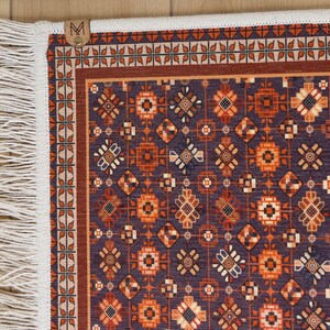 May include: A decorative rug with a geometric pattern in shades of orange, brown, and white on a dark blue background. The rug has a white fringe border.