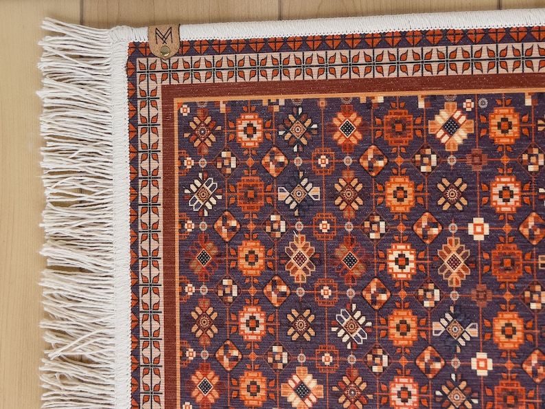 May include: A decorative rug with a geometric pattern in shades of orange, brown, and white on a dark blue background. The rug has a white fringe border.