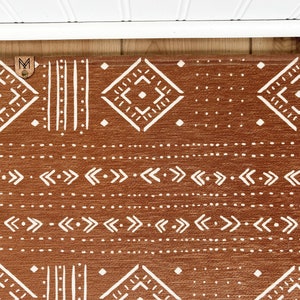 May include: A brown and white geometric patterned rug with a brown leather tag with the letter "M" on it.