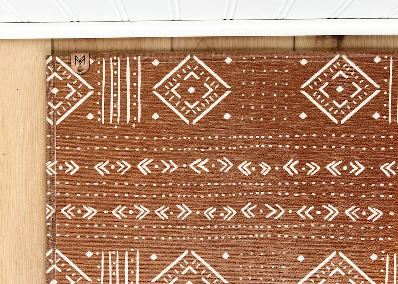 May include: A brown and white geometric patterned rug with a brown leather tag with the letter "M" on it.