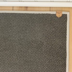 May include: A dark gray rug with a white dot pattern and a brown leather tag that says "Mission Mae" in white lettering.