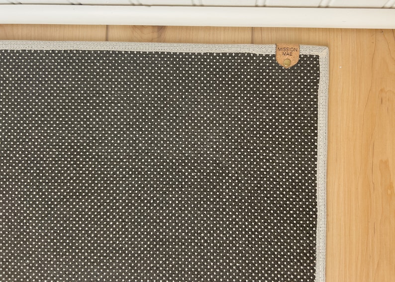 May include: A dark gray rug with a white dot pattern and a brown leather tag that says "Mission Mae" in white lettering.