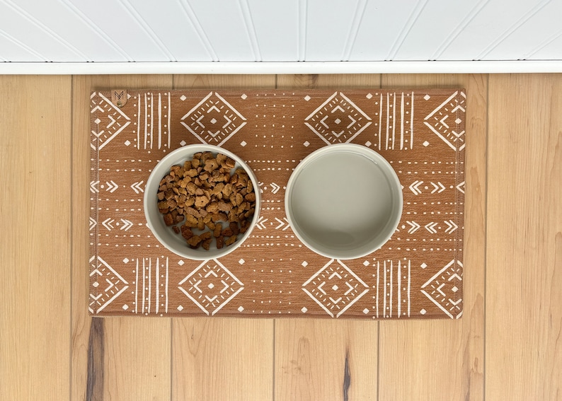May include: A brown and white patterned pet food mat with two white ceramic bowls. One bowl is filled with brown dog food.