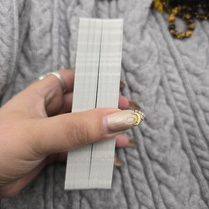 K&ouml;nnte beinhalten: Ein Tarotkartendeck, das in einer Hand gehalten wird und die Kanten der Karten zeigt. Die Karten sind wei&szlig; mit einer schwarzen Linie in der Mitte. Der Hintergrund ist ein grauer Zopfstrickpullover.