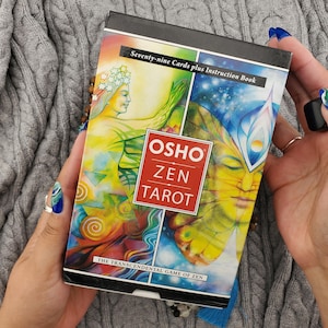 May include: A rectangular Osho Zen Tarot card deck box featuring colourful, abstract illustrations of a figure with a star crown and a face with butterfly-like wings. The text reads Seventy-nine Cards plus Instruction Book and The Transcendental Game of Zen.