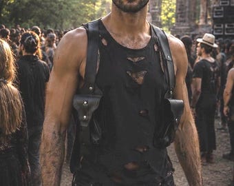 May include: A black distressed tank top with multiple rips and tears, worn with a black leather shoulder holster featuring two pouches and silver-toned metal hardware, paired with black distressed denim jeans and dark sunglasses.