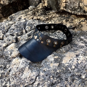 May include: A black leather visor with a wide brim and a decorative band of metal eyelets and studs.