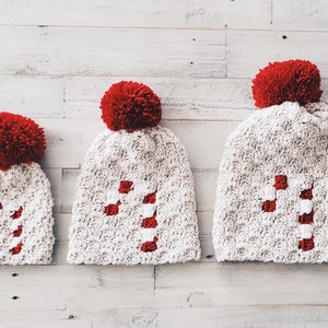 May include: Three white crocheted hats with red pom-poms and red and white candy cane designs.