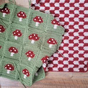 Puede incluir: Dos mantas de crochet, una verde con dise&ntilde;os de setas rojas y otra a cuadros rojos y blancos. Las mantas est&aacute;n dispuestas sobre una superficie de madera.