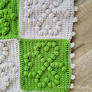 May include: Close-up of a crocheted blanket with squares in shades of green and gray. The squares have a textured, puffy design.
