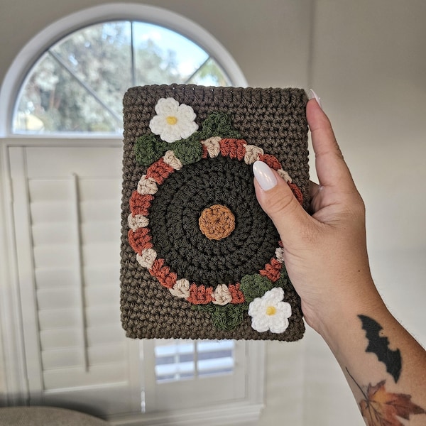 May include: A crocheted brown pouch with a circular design in shades of brown, orange, and white. The pouch is decorated with white crocheted flowers.