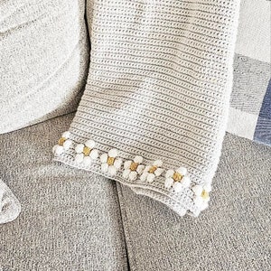 May include: A crocheted throw blanket with a white background and a border of small white and yellow crocheted flowers.